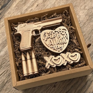 May include: A brown cardboard box filled with gold-colored items, including a gun, bullets, a heart-shaped chocolate with the text "Happy Father's Day", and a chocolate "XO" with hearts.