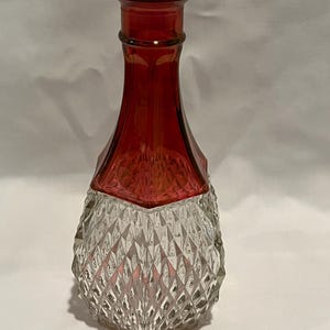 Könnte beinhalten: Eine rote Glasvase mit einem klaren, diamantförmigen Sockel.