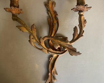 Könnte beinhalten: Antike Wandleuchte mit zwei Kerzenhaltern. Die Leuchte hat eine bronzefarbene Oberfläche mit detaillierten Blatt- und Blumendesigns. Die Kerzenhalter befinden sich am Ende geschwungener Arme. Ein klassisches Stück für die Inneneinrichtung.