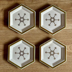 May include: Set of four hexagonal ceramic plates with a green and white border. Each plate features a stylized geometric design in black and gold.