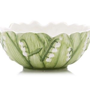 May include: A decorative ceramic bowl with a scalloped rim. The exterior is painted with green leaves and white lily of the valley flowers. The interior is white. The bowl is a light green color.
