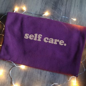 May include: A purple sweatshirt with the text "self care." in a light orange color.