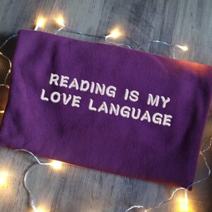 May include: A purple sweatshirt with the text "Reading is my love language" embroidered in white.