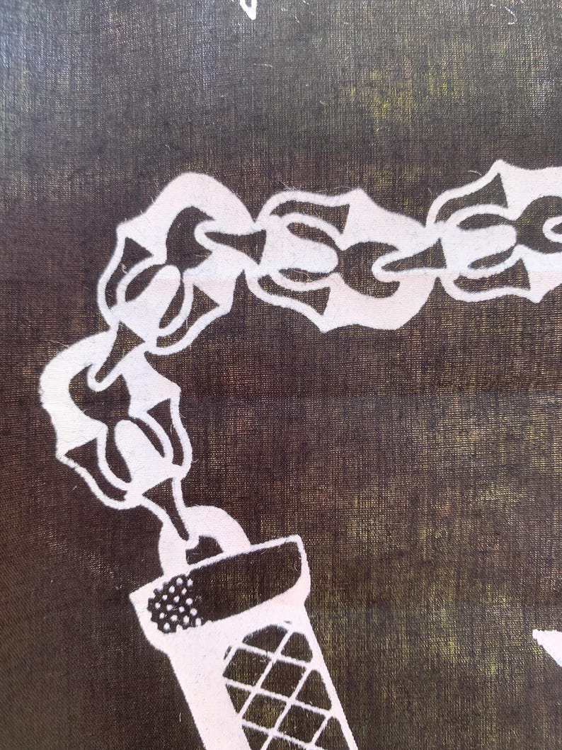 Pode incluir: Uma corrente branca com um isqueiro de metal branco preso a ela. A corrente e o isqueiro est&atilde;o sobre um fundo de tecido marrom escuro.