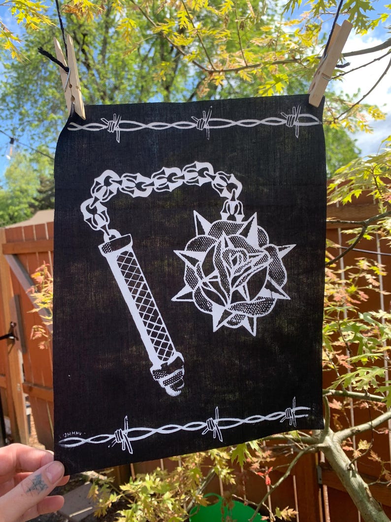 Pode incluir: Bandana preta com um desenho branco de uma clava com espinhos e uma rosa. A bandana tem uma borda de arame farpado branco.