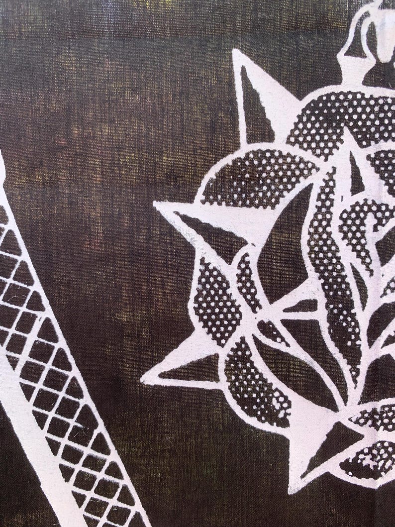 Pode incluir: Um tecido preto com um desenho branco de uma flor estilizada com uma estrela no centro. A flor tem um padr&atilde;o de pontos e &eacute; cercada por pontas afiadas.