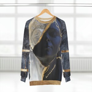 Könnte beinhalten: Ein schwarzer und goldener Pullover mit Marmormuster und einem Porträt eines Frauen Gesichts. Der Text "brown can be beautiful" ist auf dem Pullover gedruckt.