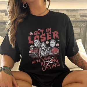 May include: Black t-shirt featuring a graphic of three horror movie characters in a car. The text on the shirt reads "Get in Loser, We're Going Killing Lifting" with the word "Killing" crossed out.