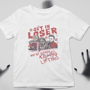 May include: White t-shirt featuring a graphic of three horror movie characters in a car. The text reads "Get in Loser, We're Going Killing Lifting".