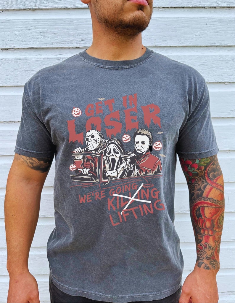 May include: A dark grey t-shirt featuring a graphic of three horror movie characters in a car. The text "Get in Loser" is above the characters and "We're going killing lifting" is below the characters. The text "killing" is crossed out.