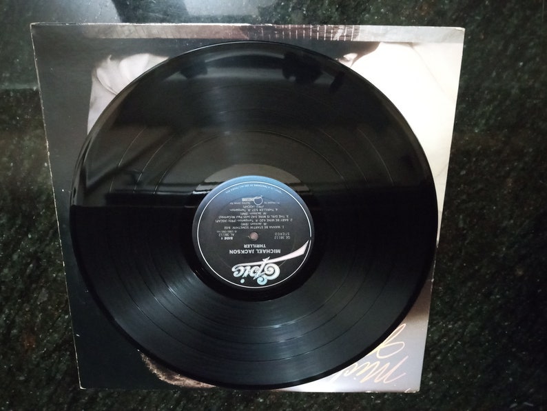 May include: Black vinyl record with a white label. The label has the text "MICHAEL JACKSON THRILLER" and the Epic Records logo.