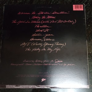 May include: Black and white vinyl record album cover with the title "Thriller" by Michael Jackson. The album cover features a close-up of Michael Jackson's face with a red background. The tracklist includes "Wanna Be Startin' Somethin'," "Baby Be Mine," "The Girl Is Mine (with Paul McCartney)," "Thriller," "Beat It," "Billie Jean," "Human Nature," "P.Y.T. (Pretty Young Thing)," and "The Lady In My Life."