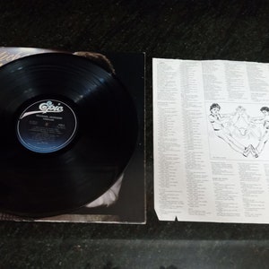 May include: A black vinyl record with a white label that says "Michael Jackson Thriller Epic" on it. The record is on a black background with a picture of Michael Jackson on the cover.