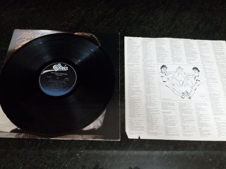 May include: A black vinyl record with a white label that says "Michael Jackson Thriller Epic" on it. The record is on a black background with a picture of Michael Jackson on the cover.