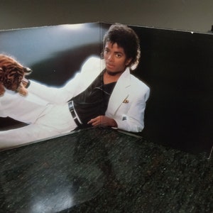 May include: A black and white photo of a man wearing a white suit jacket and a black shirt, holding a tiger cub.