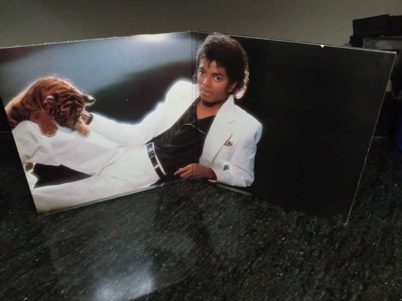 May include: A black and white photo of a man wearing a white suit jacket and a black shirt, holding a tiger cub.