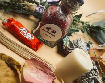 May include: A small glass bottle with a red liquid and a label that reads "Dragon Lair Protection Potion". The bottle is surrounded by dried flowers, a candle, and a chocolate bar.
