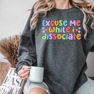 May include: A dark grey sweatshirt with the text "Excuse me while I dissociate" in colourful letters with flowers around the text.