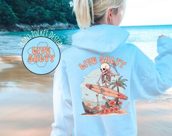 May include: A light blue hoodie with a graphic of a skeleton surfing on a surfboard with the text "Live Salty" on the back. The hoodie has a front pocket with the text "Live Salty" in a circle.