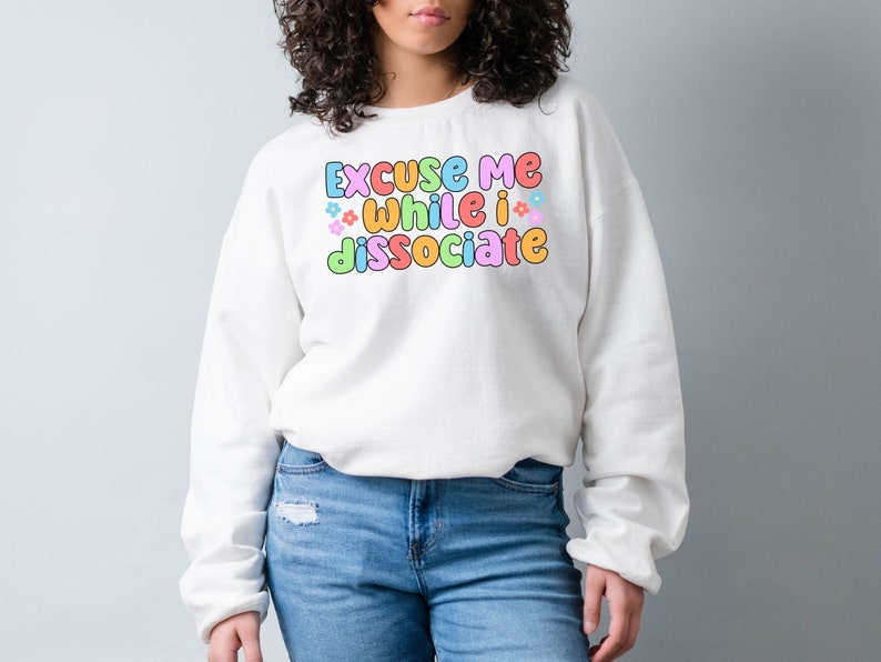 May include: White sweatshirt with the text "Excuse me while I dissociate" in colourful bubble letters with small flower accents.