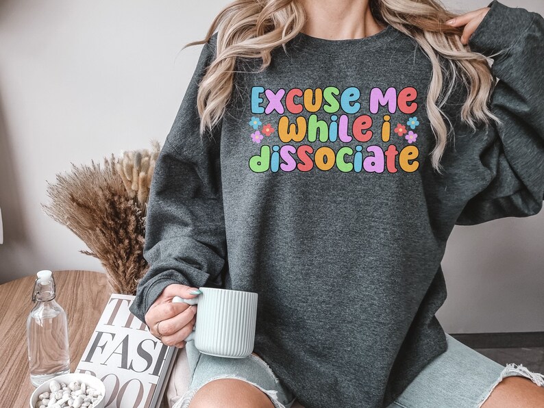 May include: A dark grey sweatshirt with the text "Excuse me while I dissociate" in colourful letters with flowers around the text.