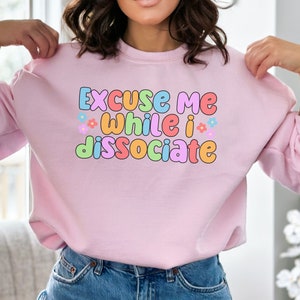 May include: Pink sweatshirt with the text "Excuse me while I dissociate" in colourful letters with small flower accents.