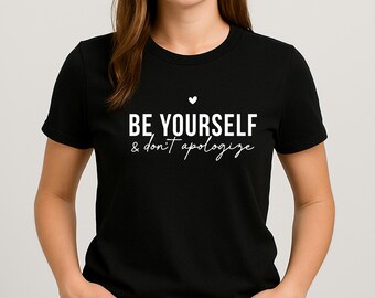 May include: Black t-shirt with the white text "BE YOURSELF & don't apologize". The text is centered on the chest, with a small heart above the words. The shirt is a crew neck style.