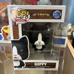 May include: A Funko Pop! vinyl figure of Guppy from The Binding of Isaac: Rebirth. The figure is black and white with a cat-like appearance, packaged in a clear display box. The box features the Funko Pop! Games logo and the number 1179.