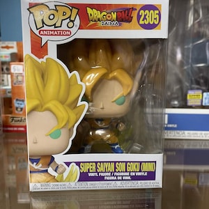 May include: A Super Saiyan Son Goku (Mini) vinyl figure from the Dragon Ball Daima series, packaged in a clear display box. The figure has yellow hair and a blue and orange outfit. The box features the Pop! Animation logo.
