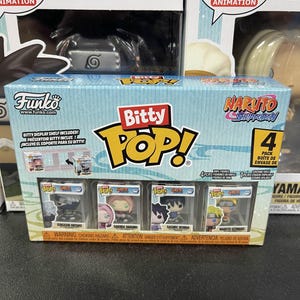 May include: A Funko Bitty Pop! 4-pack featuring characters from Naruto Shippuden. The box includes Kakashi Hatake, Sakura Haruno, Sasuke Uchiha, and Naruto Uzumaki figures. The packaging has a blue and white design with the words "Bitty Pop!" in a yellow bubble.