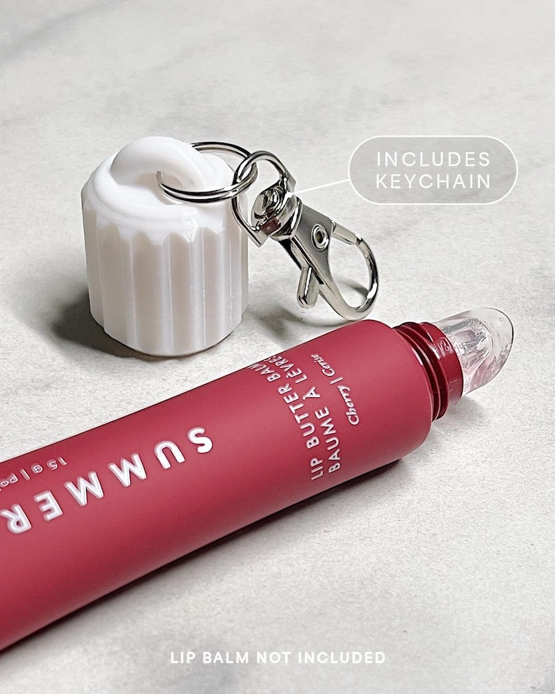 May include: A pink lip balm tube with the word "SUMMER" printed on it. The tube has a clear applicator tip and a silver keychain attached to the cap. The text "LIP BUTTER BALM BAUME A LEVRE Cherry | Cerise" is printed on the tube. The text "INCLUDES KEYCHAIN" is printed on a white background.