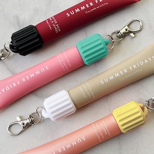 May include: Four tubes of Summer Fridays lip butter balm in different colours, each with a coloured cap and a silver clip. The tubes are labelled with the brand name and product details. The colours include red, pink, beige, and peach.