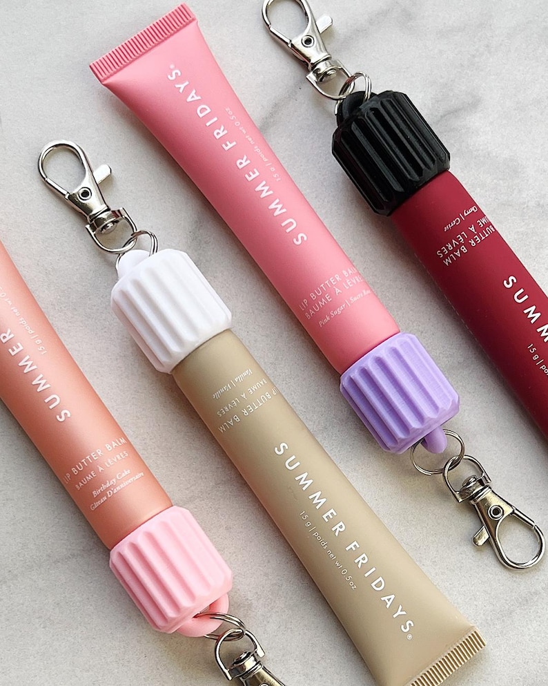 May include: Four lip balm tubes with keychains. The tubes are labeled "Summer Fridays" and are in the colors pink, beige, purple, and red. The lip balms are labeled "Lip Butter Balm" and "Baume a Levres".