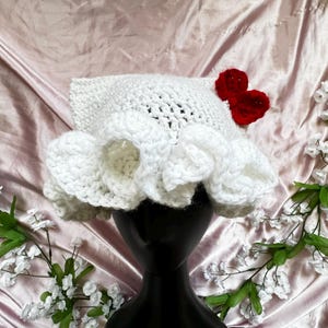 May include: White crocheted hat with a ruffled brim and two red felt hearts attached to the side.