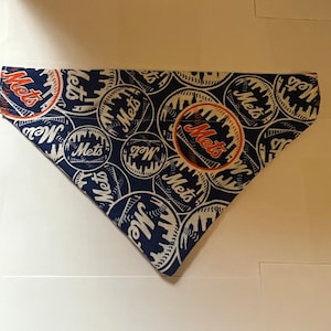 May include: A blue and white bandana with a repeating pattern of the New York Mets logo. The logo features the team's name in orange and white text, with a baseball and the New York City skyline in the background.