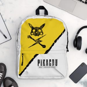 Może przedstawiać: Biały plecak z żółtym panelem z czarnym wzorem czaszki i skrzyżowanych piszczeli Pikachu. Plecak ma czarny zamek błyskawiczny, a słowo "PIKACHU" jest wydrukowane na czarno. Widoczne są również czarne trampki, słuchawki i laptop.