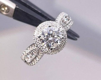 May include: A silver engagement ring with a large round center diamond surrounded by smaller diamonds. The ring has a delicate, twisted band.