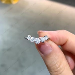 Pode incluir: Um anel de prata com cinco diamantes redondos engastados em um design curvo e arqueado.