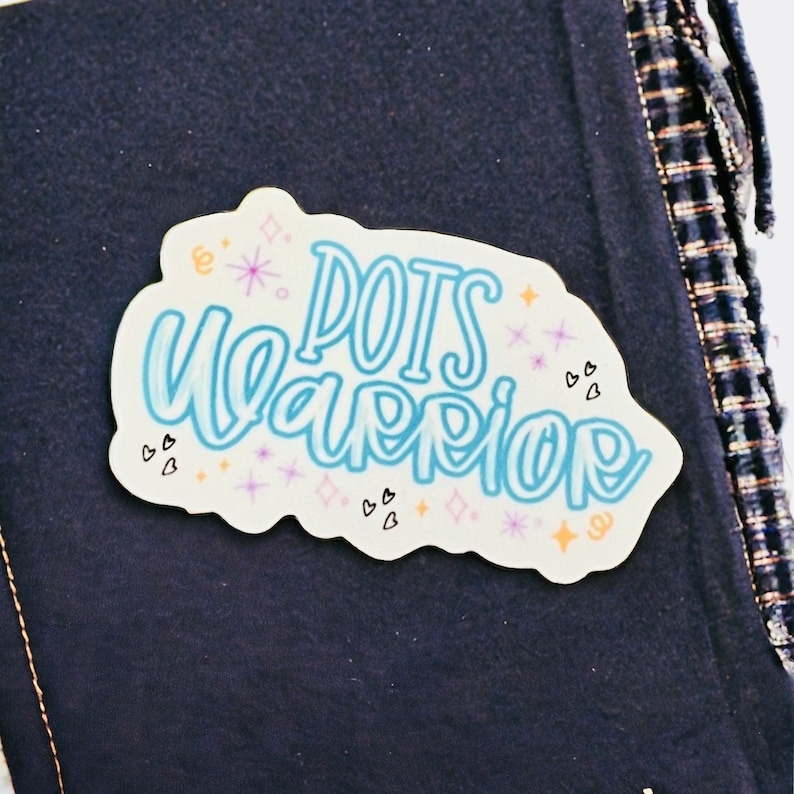 May include: A white sticker with blue lettering that says "POTS Warrior" with a sparkly design. The sticker is on a dark blue fabric background.