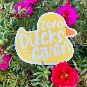 May include: A yellow rubber duck sticker with the text "zero ducks given" in white lettering. The sticker is on a background of pink and green flowers.
