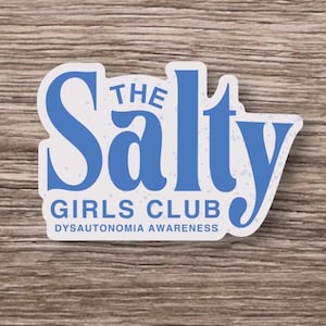Può includere: Un adesivo bianco con testo blu che recita "The Salty Girls Club" con "Dysautonomia Awareness" in basso. L'adesivo ha un bordo blu e si trova su uno sfondo di venature del legno.