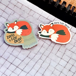 May include: Two fox stickers with the text "Zero Fox Given". The fox on the left is curled up in a blanket with a paw sticking out. The fox on the right is curled up in a sleeping position.