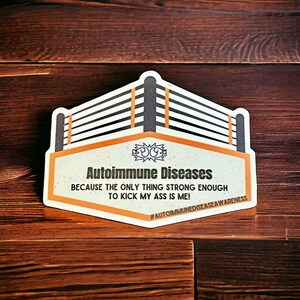 Peut inclure: Un autocollant avec un graphique de ring de lutte et le texte "Autoimmune Diseases Because the only thing strong enough to kick my ass is me! #AutoimmuneDiseaseAwareness".