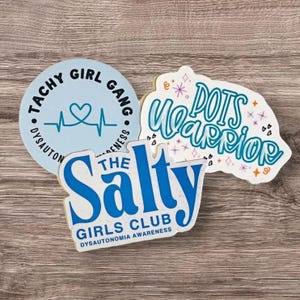 May include: Three stickers with blue text on a light wood background. The first sticker is light blue with a heart and a heartbeat line and the text "Tachy Girl Gang Dysautonomia Awareness". The second sticker is white with blue text and the words "The Salty Girls Club Dysautonomia Awareness". The third sticker is white with blue text and the words "POTS Warrior" with pink and purple stars and hearts.