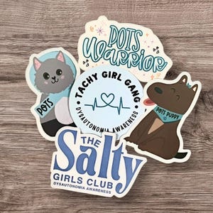 May include: Four stickers with blue and white designs. One sticker features a cat with the text "POTS" and a heart. Another sticker features a dog with the text "POTS PUPPY". A third sticker features a heart with the text "TACHY GIRL GANG" and "DYSAUTONOMIA AWARENESS". The fourth sticker features the text "THE Salty GIRLS CLUB" and "DYSAUTONOMIA AWARENESS".