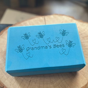 May include: A light blue rectangular block with the text "Grandma's Bees" and five bees with hearts printed on it.