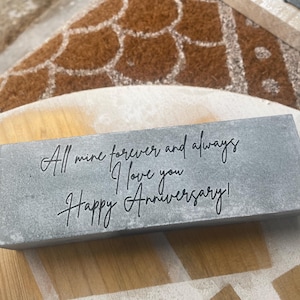 Op de afbeelding: Een grijze stenen blok met de inscriptie "All mine forever and always I love you Happy Anniversary!" in zwarte letters.