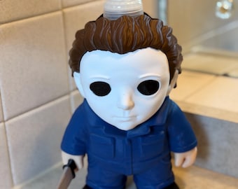 May include: A soap dispenser shaped like a character with a white mask, brown hair, and a blue jumpsuit. The figure has black eyes and holds a small silver-colored knife in one hand. A clear plastic pump mechanism is attached to the top of the head.