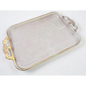 May include: A rectangular silver serving tray with gold trim and handles. The tray has a delicate floral pattern across the surface. The handles have a decorative design. The tray is suitable for serving food and drinks.