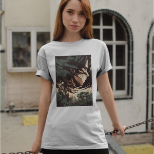 May include: A white t-shirt with a graphic print of a character from the anime Attack on Titan. The character is depicted in a forest setting with a sunset in the background.